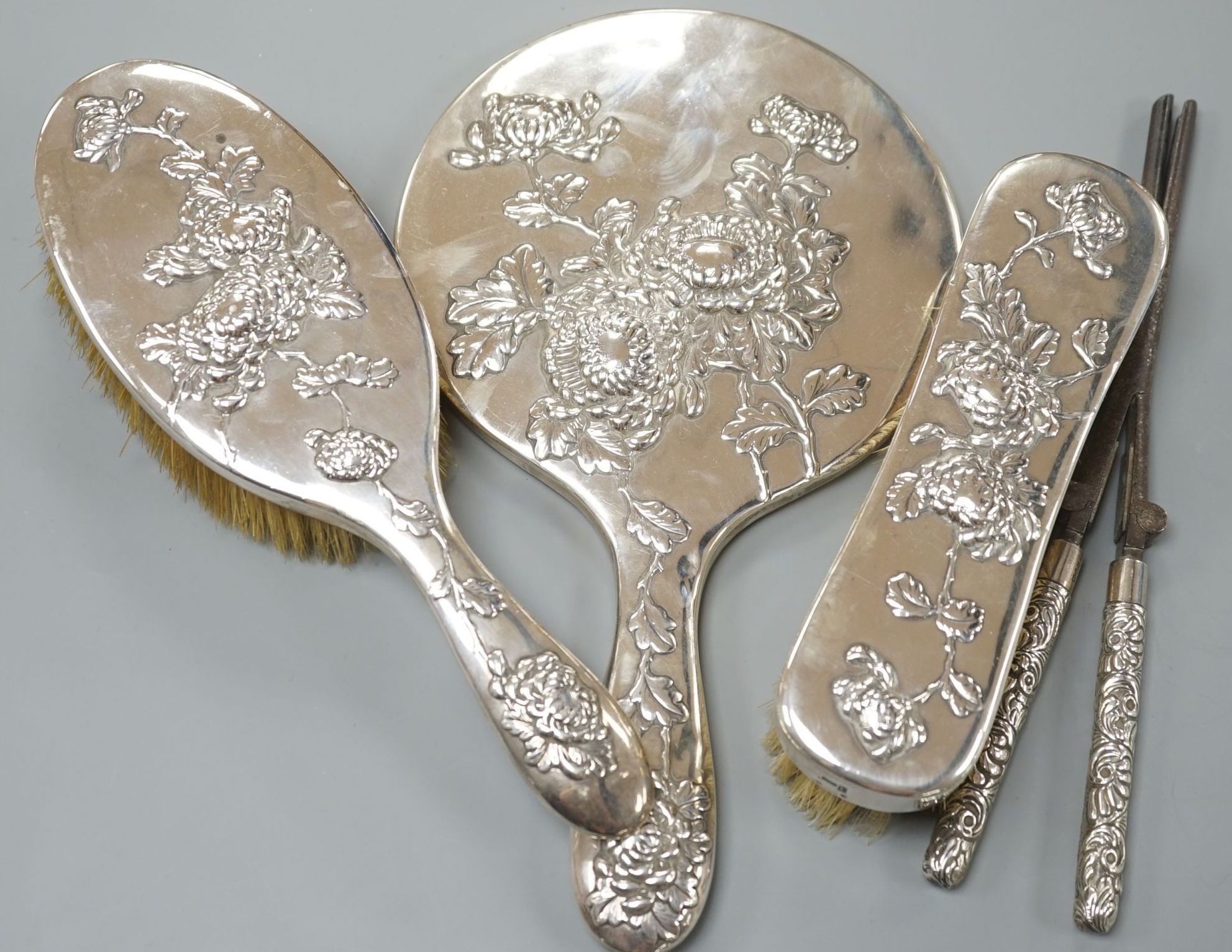 An early 20th century Chinese Export white metal three piece dressing table set, by Wang Hing, Hong Kong, comprising a mirror and two brushes and a pair of associated silver handled curling tongs.